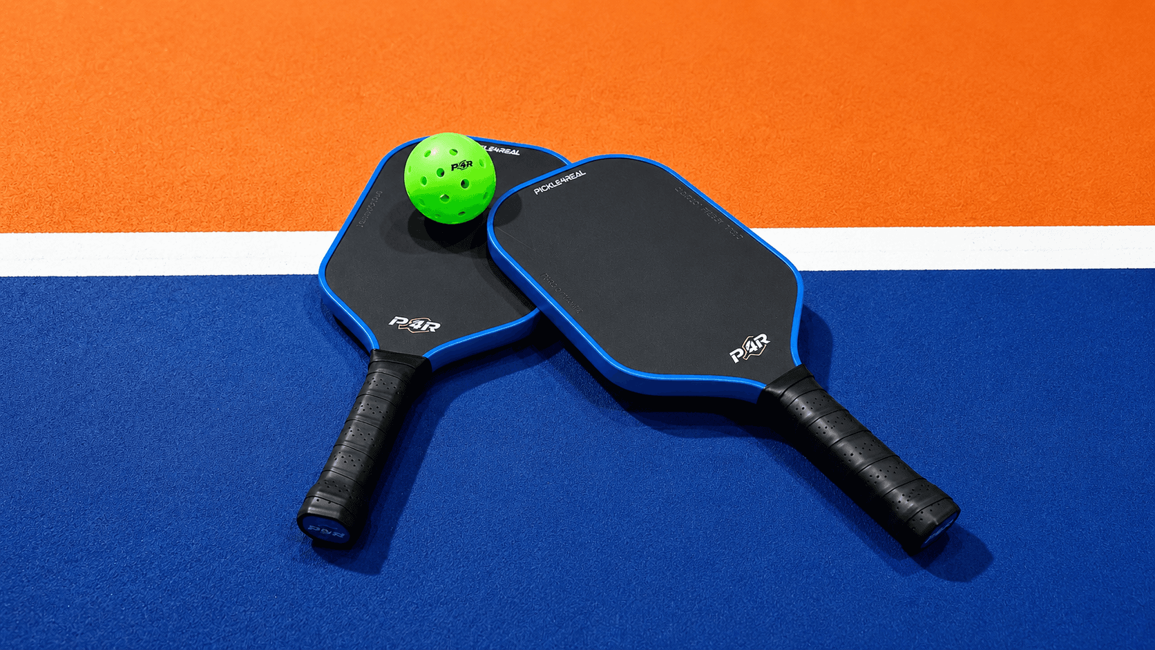 Two Pickle4Real branded paddles and a ball on the court